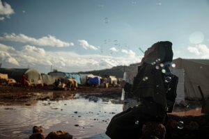 A woman in a hijab joyfully blows bubbles in a refugee camp in Idlib, Syria.